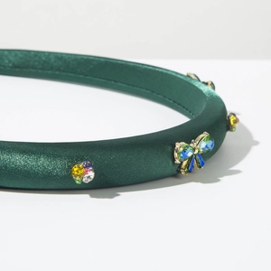 Détail du serre-tête en satin vert forêt avec nœud en strass colorés et motifs floraux