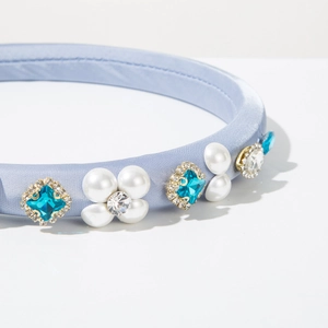 Close-up of light blue satin headband with blue rhinestones and white pearls detail