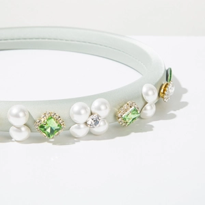 Detail of light green satin headband with pearls and green gemstones in gold settings