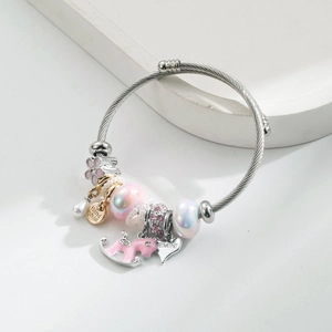 Detail of silver cable bracelet with pink enamel flower and heart charms in soft lighting