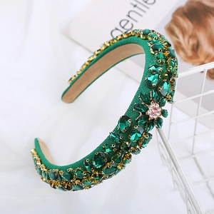 Detail of emerald green crystal headband with intricate gold claw settings and pink floral accent
