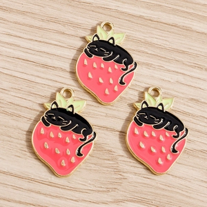Detailed view of three enamel black cat and strawberry charms on a light wood background