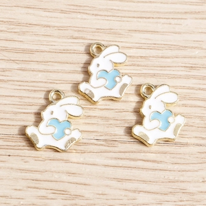 Three white enamel bunny charms with blue hearts on a natural wood surface for DIY jewelry