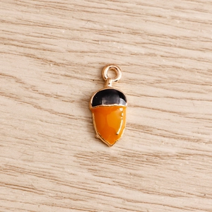 Detailed view of handmade enamel acorn charms with bright orange finish and gold edges