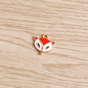 Détail d'une breloque tête de renard en émail orange et blanc avec finition dorée