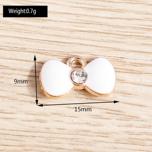 Detailed view of white enamel bow pendant with gold trim and crystal, 9mm by 15mm