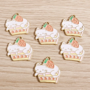 Cute enamel cat on strawberry cake charms with gold plating on a wooden background