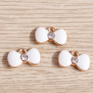 Detailed macro view of white enamel bow charms with rose gold edges and sparkling crystals