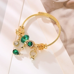 Gold-plated charm bracelet with green emerald beads and a sparkling swan pendant