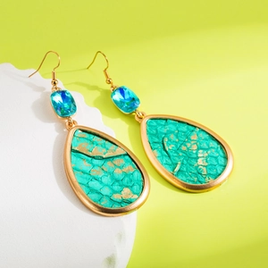 Golden teardrop earrings with green python texture and blue crystal gems on white stone