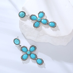 Detail of silver cross drop earrings with turquoise inlays on white stone decor