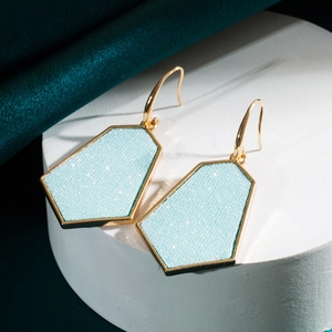 Macro-detail van geometrische vijfhoekige oorbellen met lichtblauwe glitter en goud