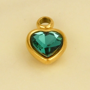 Macro detail of a heart-shaped golden pendant with a dark green faceted crystal