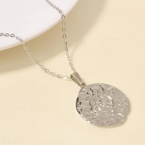 Detailed close-up of a silver sunburst pendant with unique hammered metal texture and chain
