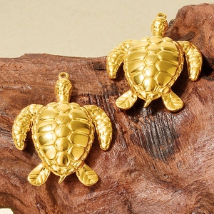 Detailed macro of two gold sea turtle pendants with polished texture on dark wood base