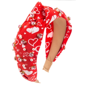 Détail d'un bandeau noué rouge avec motifs cœurs blancs, strass roses et perles élégantes