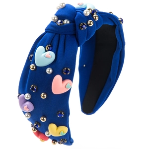Détail d'un serre-tête noué bleu foncé avec cœurs pastel, perles et cristaux