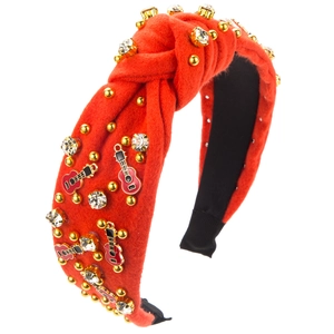 Détail d'un serre-tête en tissu rouge avec breloques de violon dorées et strass brillants