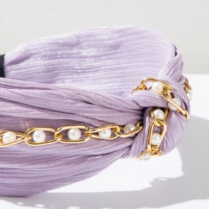 Detailaufnahme des lavendelfarbenen Haarreifs mit Goldkette und weißen Kunstperlen