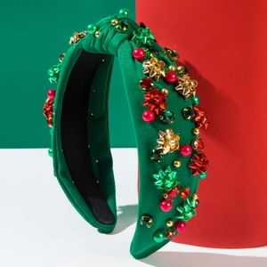 Cerchietto natalizio in tessuto verde con fiocchi e cristalli rossi su sfondo festivo