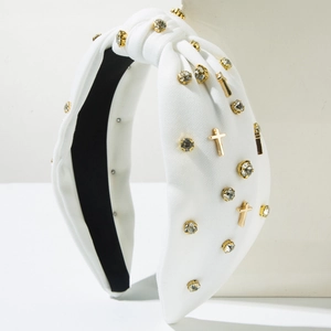 White knotted fabric headband with gold rhinestones and cross charms on white pedestal
