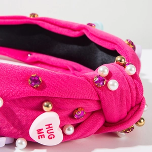 Gros plan sur serre-tête rose noué avec strass, perles et un pendentif cœur Hug Me