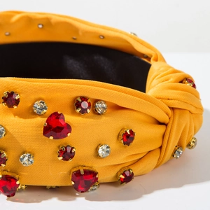 Close-up of mustard yellow headband with red heart rhinestones and gold claw settings