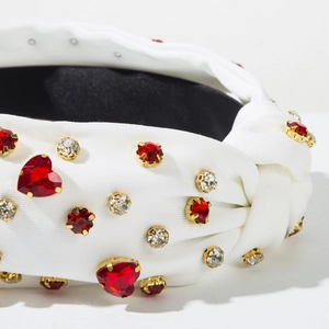 Close-up of white ribbed headband with red heart-shaped rhinestones and knot detail