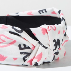 Detailed view of white fabric headband featuring pink hearts, LOVE text, and a knotted design