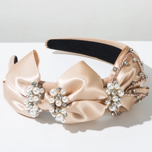 Gros plan du serre-tête en satin champagne avec nœud élégant en perles et strass brillants