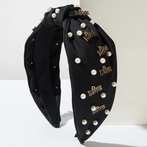 Détail d'un serre-tête noir noué avec des perles blanches et des lettres LOVE dorées