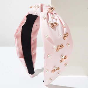 Détail du serre-tête noué rose avec perles blanches et lettrage LOVE doré élégant