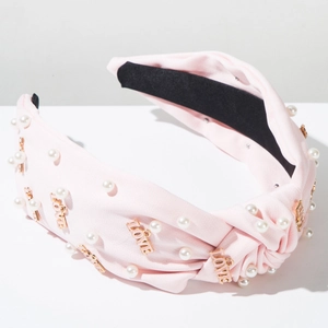 Détail d'un serre-tête en tissu rose avec perles blanches et breloques LOVE dorées
