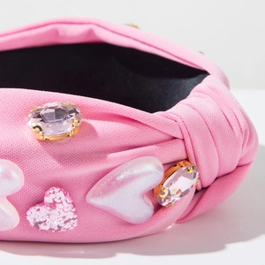 Detail eines rosa geknoteten Stirnbands mit herzförmigen Akzenten und Strassverzierungen