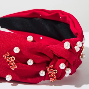 Détail d'un serre-tête en tissu rouge avec perles et breloques LOVE dorées pour femme