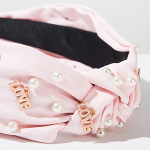 Détail d'un serre-tête en tissu rose avec perles blanches et breloques LOVE