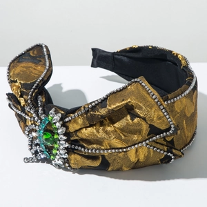 Détail d'un serre-tête large de luxe avec jacquard doré et broche vintage en émeraude