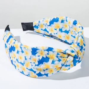 Detail of blue knotted headband with yellow plumeria floral print on a white pedestal