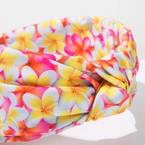 Close-up of bohemian fabric headband featuring a tropical frangipani floral print and twist detail