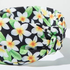 Close-up of bohemian wide knotted headband with white plumeria floral print on black fabric