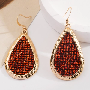 Close-up of teardrop earrings with red sequins and hammered gold metal finish