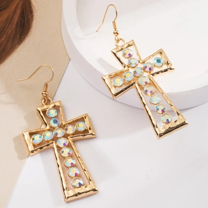 Detalle de pendientes de cruz dorados con brillantes diamantes AB sobre bandeja de piedra blanca