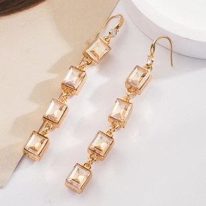 Boucles d'oreilles bohèmes dorées avec cristaux champagne sur un support élégant blanc