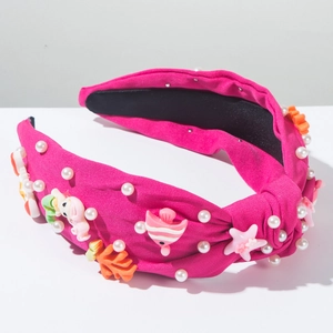 Détail d'un serre-tête à nœud magenta orné de perles blanches et de breloques marines