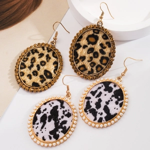 Close-up of leopard and cow print oval earrings with rhinestone and pearl borders