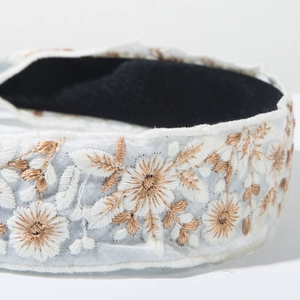 Macro detail of bohemian floral embroidery with golden silk thread on white satin headband