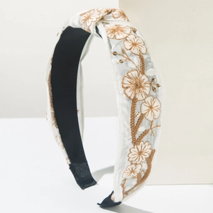 Detail of white wide knotted headband with intricate brown floral embroidery and gold sequins