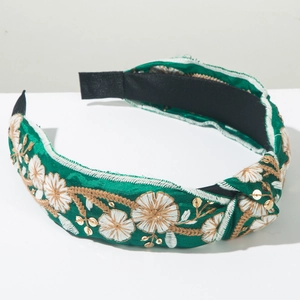 Detail of green knotted headband with white floral embroidery and golden sequins