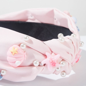 Détail d'un serre-tête rose torsadé avec coquillages en résine, étoiles de mer et perles