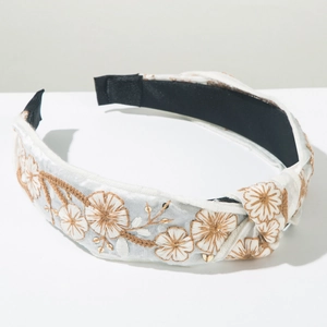 Close-up of white satin headband featuring floral embroidery and gold sequins detail